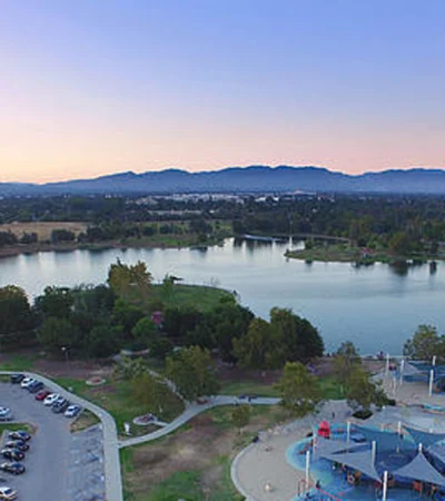 a lake with a parking lot and a park with trees and a mountain in the background