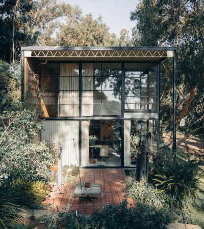 a small house with a lot of plants and trees around it
