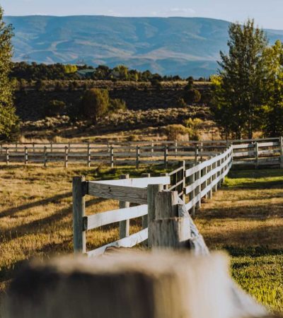 a wooden fence in a field with mountains in the background