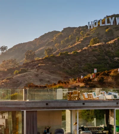 a building with a glass balcony overlooking a hill with trees and a sign