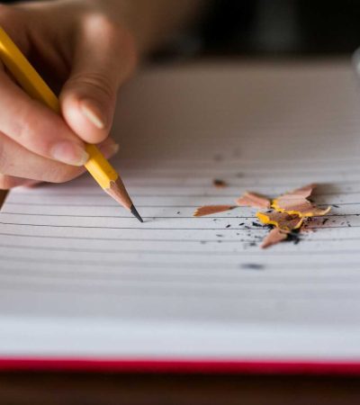 person holding pencil writing on notebook